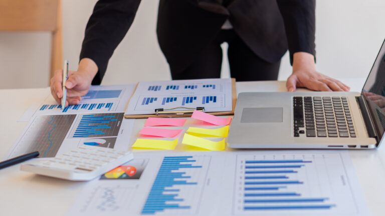 Pessoa analisando gráficos financeiros e gerenciando múltiplos CNPJs em um ambiente corporativo com laptop e relatórios.