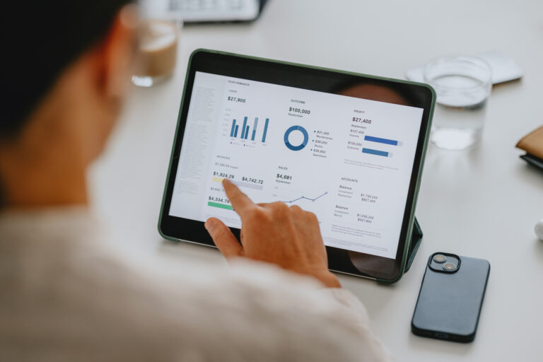 Pessoa analisando indicadores financeiros em tablet, com gráficos de desempenho, lucros, vendas e contas.