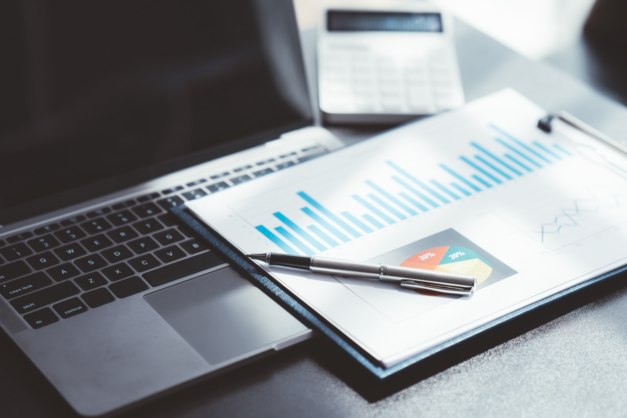 Relatório financeiro com gráficos de barras e pizza sobre notebook, representando análise de desempenho empresarial.